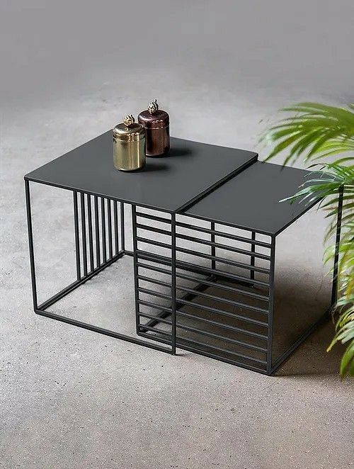 Modern black metal side table with a plant on a gray concrete floor